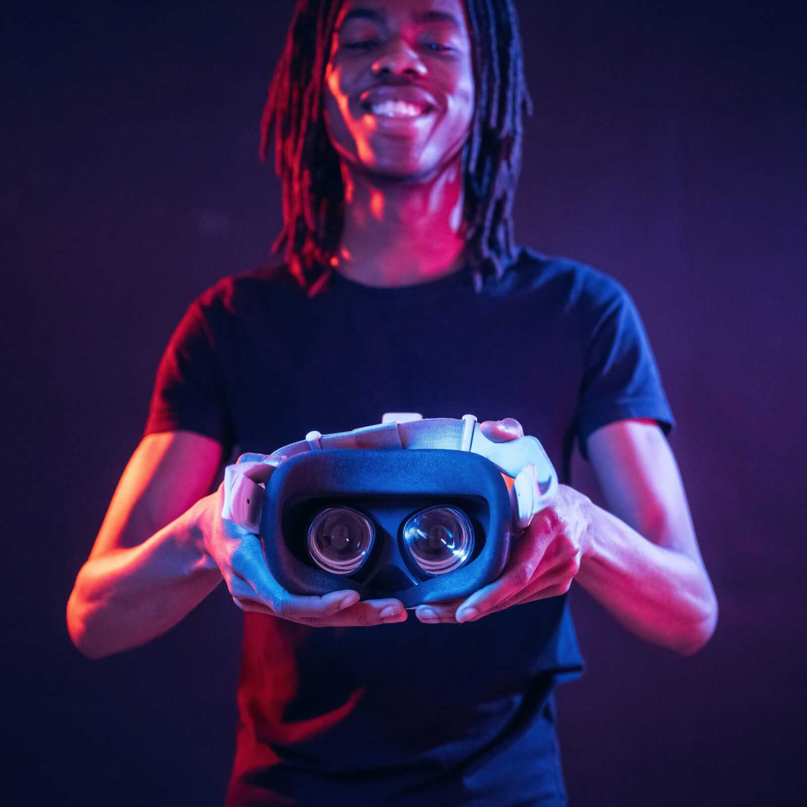 Smiling, positive facial expression. African American guy is with virtual reality glasses in neon room