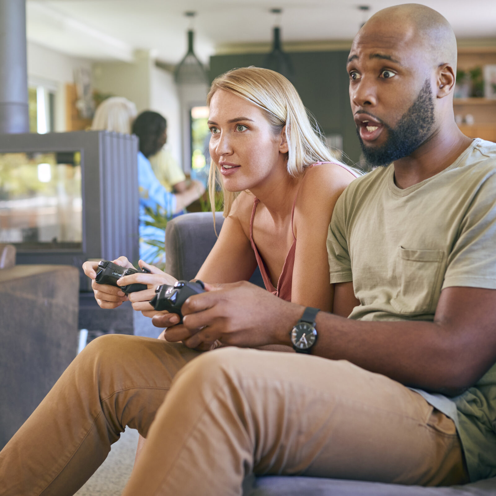 Couple On Sofa At Home Together Playing Computer Game With Multi-Generation Family In Background